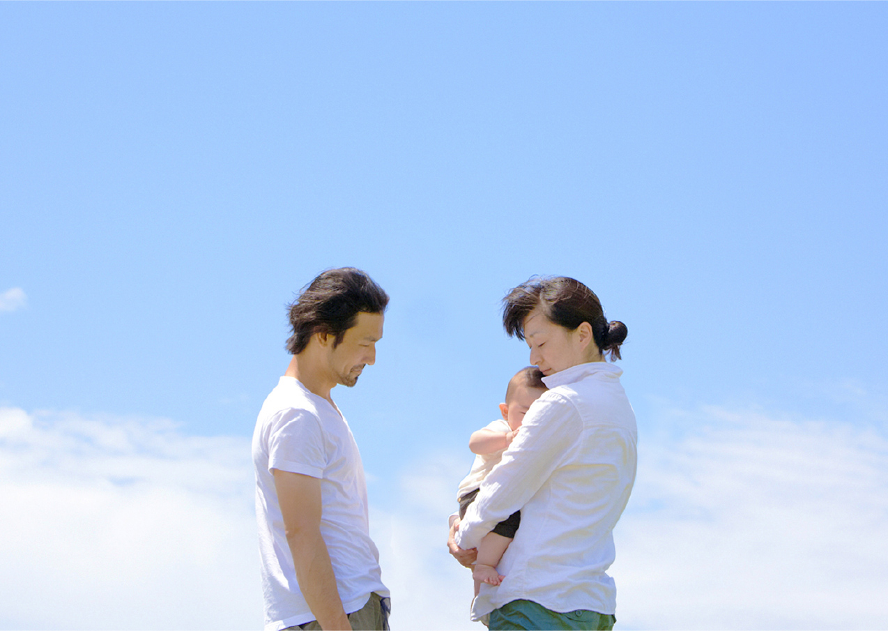 青空の下子供を抱く夫婦